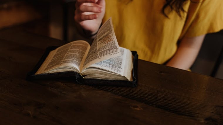 person reading Bible on top of brown wooden table