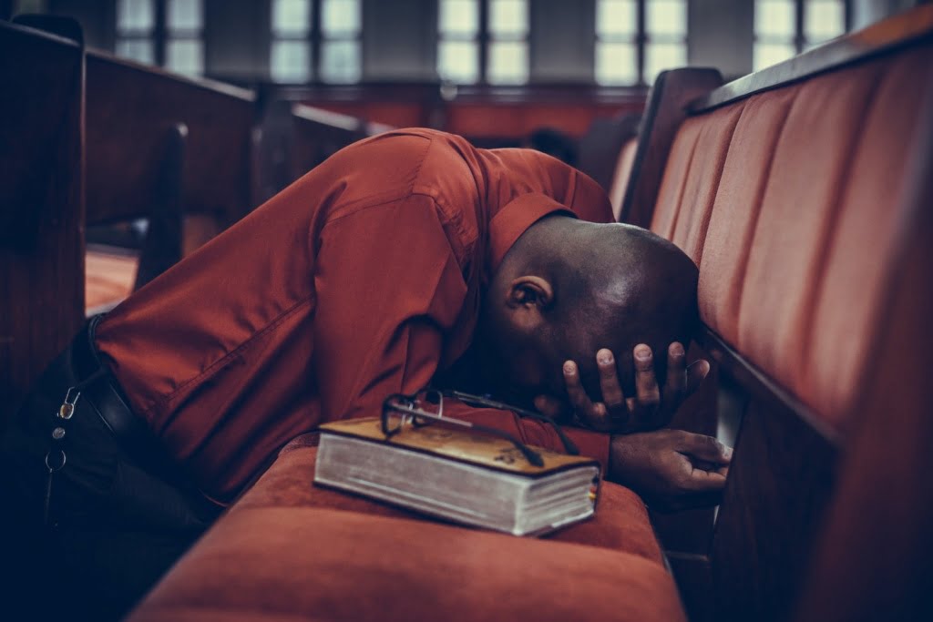 pray again, man in orange top beside eyeglasses on brown book